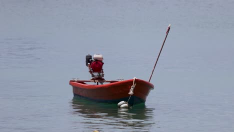 a red longtail boat gently floats on calm waters in phuket, thailand, under soft daylight, showcasing serene maritime scenery