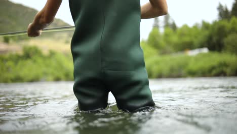 Slow-Motion-Shot-of-a-male-fisherman-wearing-waders-while-Fly-Fishing