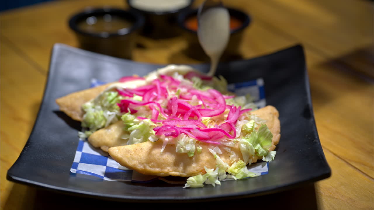 cámara lenta de cerca de las empanadas tradicionales mexicanas con lechuga picada y cebolla roja en la parte superior y alguien vertiendo crema agria sobre ellos