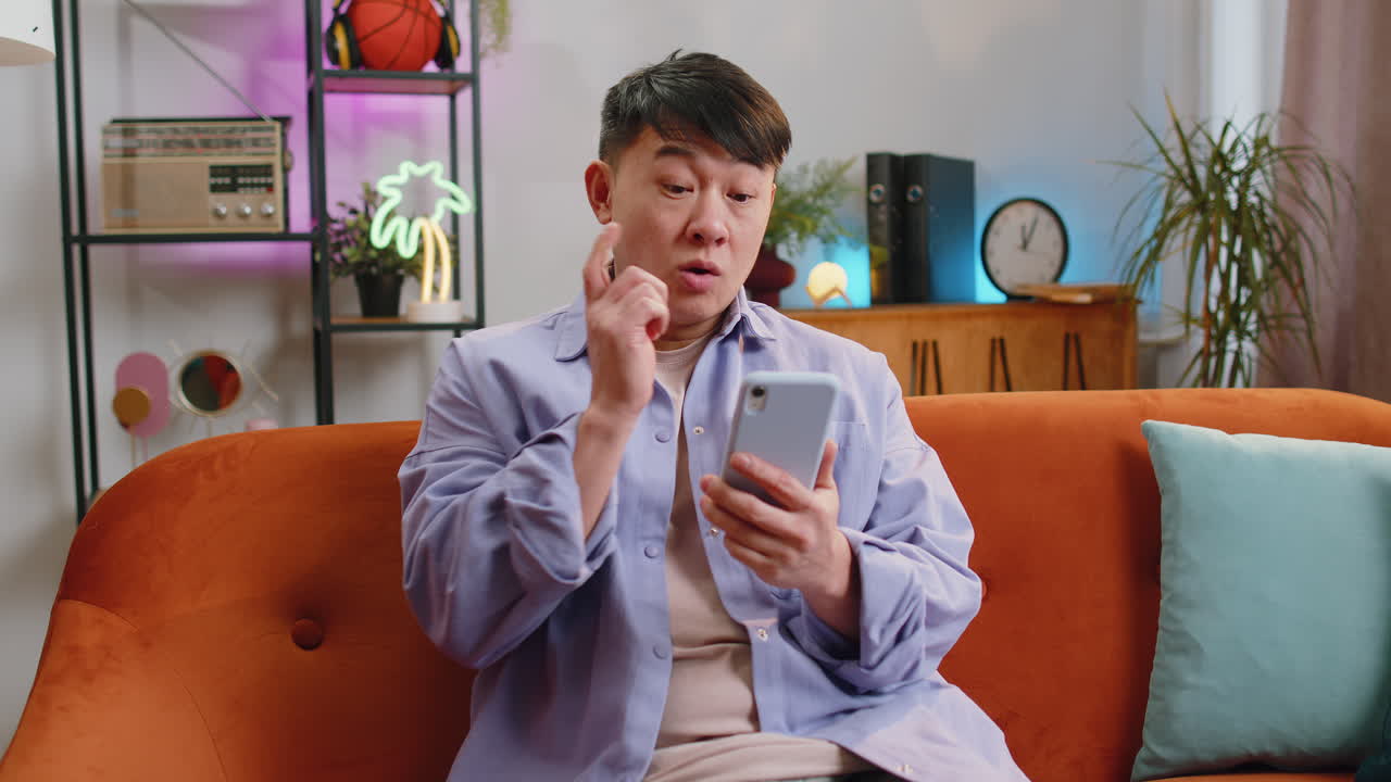 Asian chinese adult man sitting on sofa using smartphone share messages on social media application