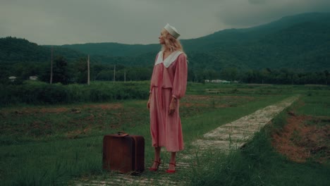 woman in vintage dress with suitcase in the countryside