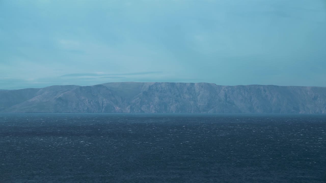 크로아티아의 크르크 섬과 은 파란 물과 함께 크로아시아의 지중해 해변에서 작은 파도와 함께 경치가 아름다운 자연의 움직이는 물 바다를 지평선으로 바라보고 있습니다. 야외 관광 휴가 해가 지는 시네마그래프 4k에서 원활한 비디오 루프.