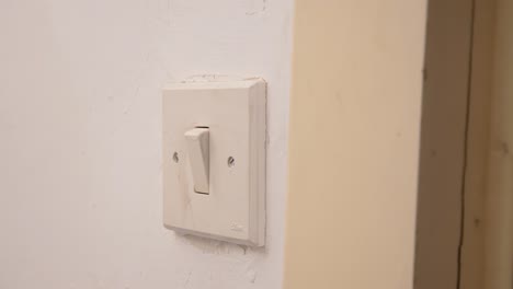 encendiendo y apagando delicadamente con un dedo un viejo interruptor de luz desgastado, manipulando el mecanismo envejecido