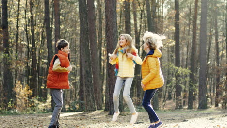 close-up view of joyful kids, girl and two boys, laughing, jumping and having fun in the forest on a sunny day