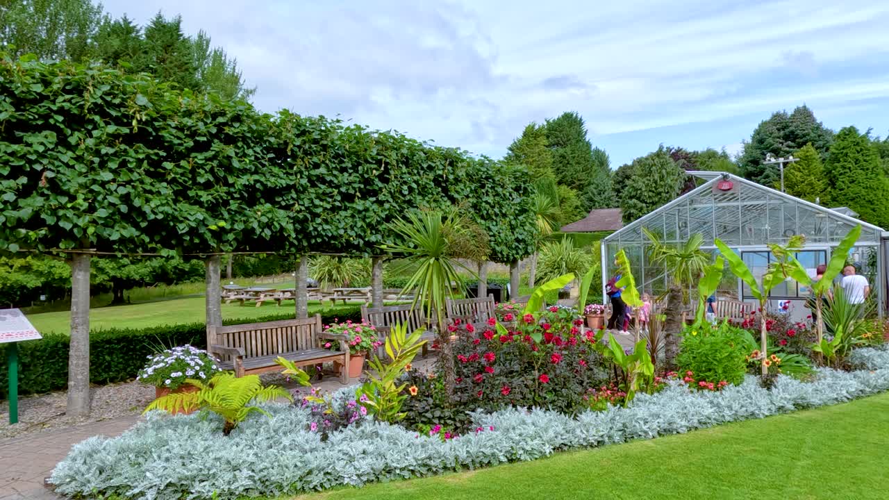 Daylight camera pan reveals vibrant flower beds, manicured hedges, and greenhouse structures in a lush botanical garden setting in Durham, England