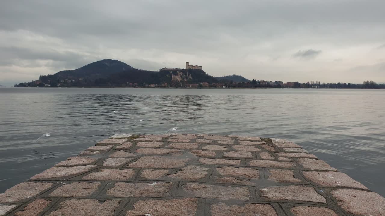 las gaviotas vuelan lejos del muelle con vistas al lago maggiore y a la fortaleza de angrya