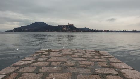 seagulls fly away from pier overlooking maggiore lake and angera fortress