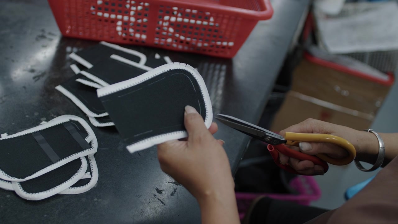 Worker hand-cutting shoe components at a table in a footwear production facility
