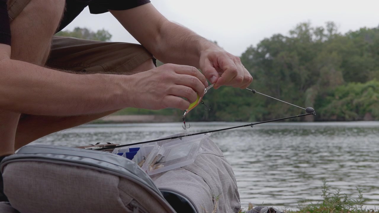Seorang pemuda dengan hati-hati menyiapkan tali pancingnya, fokus mempersiapkan hari memancing yang sukses, dengan danau yang tenang menyediakan latar belakang yang indah