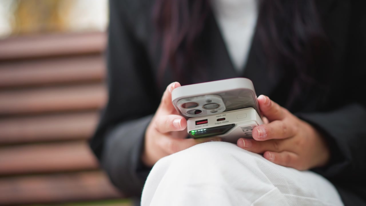 Close up of woman holding and using smartphone with both hands while seated on steps. scene features soft natural light focusing solely on interaction between woman fingers and device