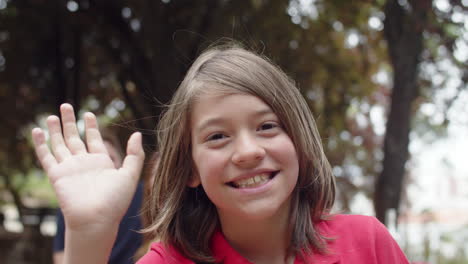 close-up shot of young boy looking at camera, waving hand and smiling