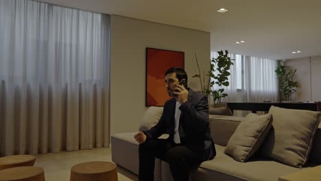 confident executive man making a business call while sitting on a stylish couch in a modern office, shot with a smooth zoom out.