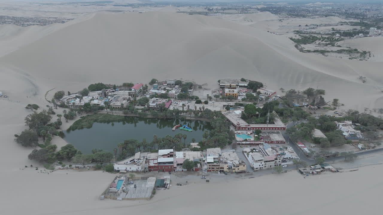 Drone shot revealing the city of Huacachina in Peru behind the dunes on a cloudy morning during the mist LOG