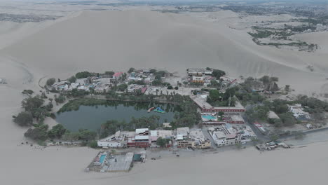 Drone shot revealing the city of Huacachina in Peru behind the dunes on a cloudy morning during the mist LOG