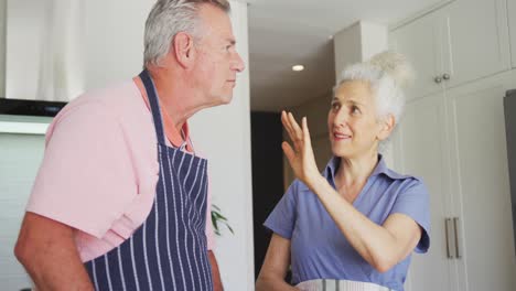 Glückliches-Kaukasisches-älteres-Paar-Mit-Schürzen,-Das-Gemeinsam-In-Der-Küche-Kocht