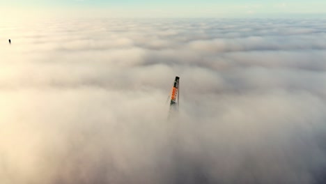 construction crane arm emerging through dense morning fog during sunrise, aerial overview