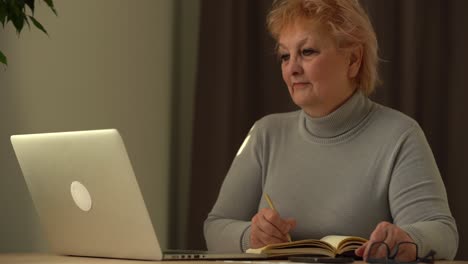 Close-up-wrinkled-male-hands-writing-information.-Old-mature-woman-working-at-office,-using-computer,-handwriting-notes