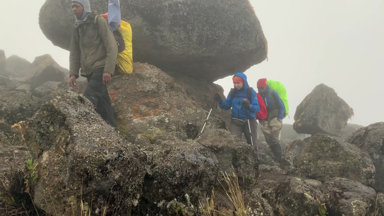 Side view of tourists with backpacks walking step by step through the wasteland between the rocks in the fog