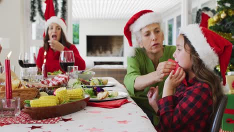 abuela caucásica feliz limpiando la boca de su nieta en la mesa de navidad