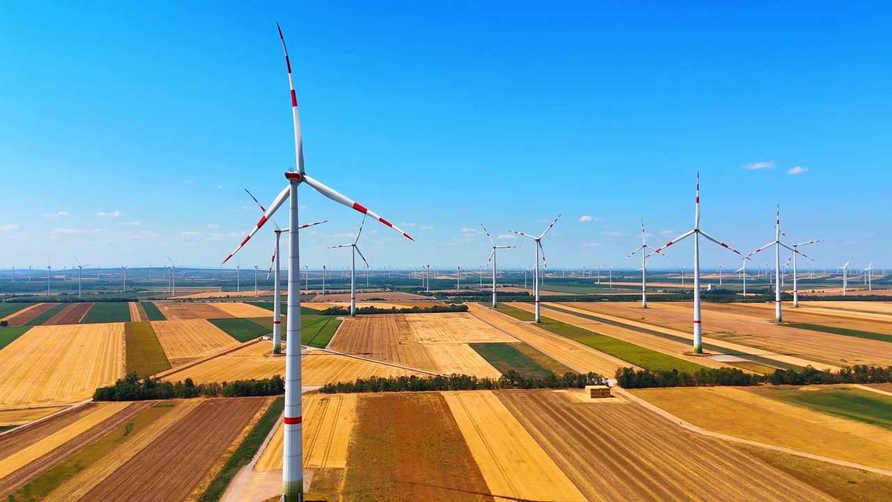 Duurzame energieturbines die staan in kleurrijke velden onder de lucht. Breed luchtbeeld van een ecologische energiecentrale boven gestreepte gele en groene akkerlanden.