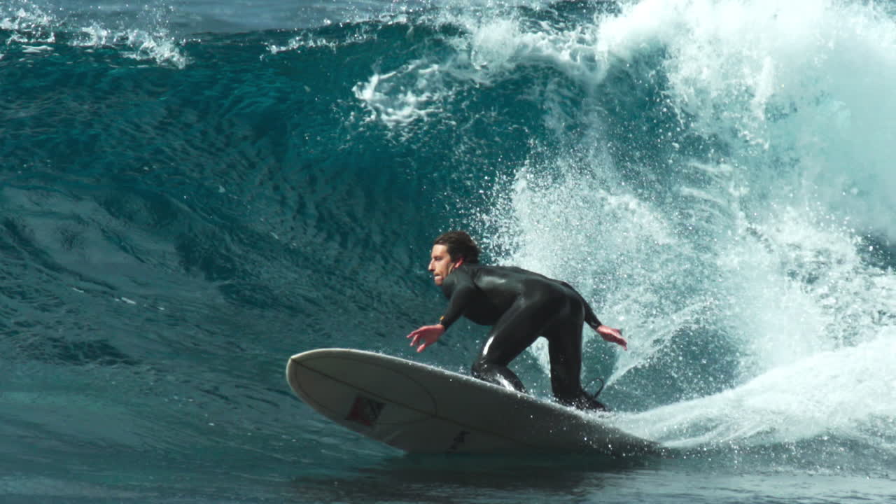 Slow motion telephoto of longboard surfer rising up to top and cutting back off lip of wave
