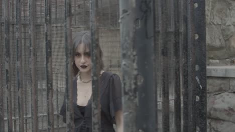 slow motion shot of a goth girl behind rusted animal cage bars