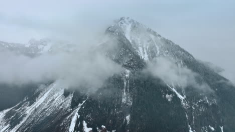 High mountain with pine-trees growing on and snow covering some parts of it. White mist coating the mount.