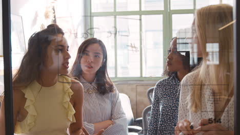 Four-female-creatives-brainstorming-ideas-onto-a-glass-wall