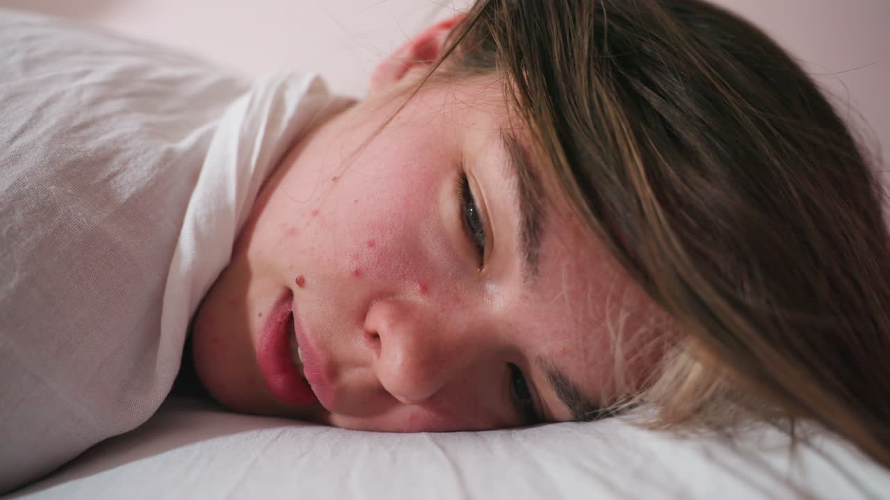Close-up view of female client with blonde hair lying sideways with relaxed expression, face gently resting on soft white bed linen, creating serene and intimate indoor atmosphere in tranquil setting