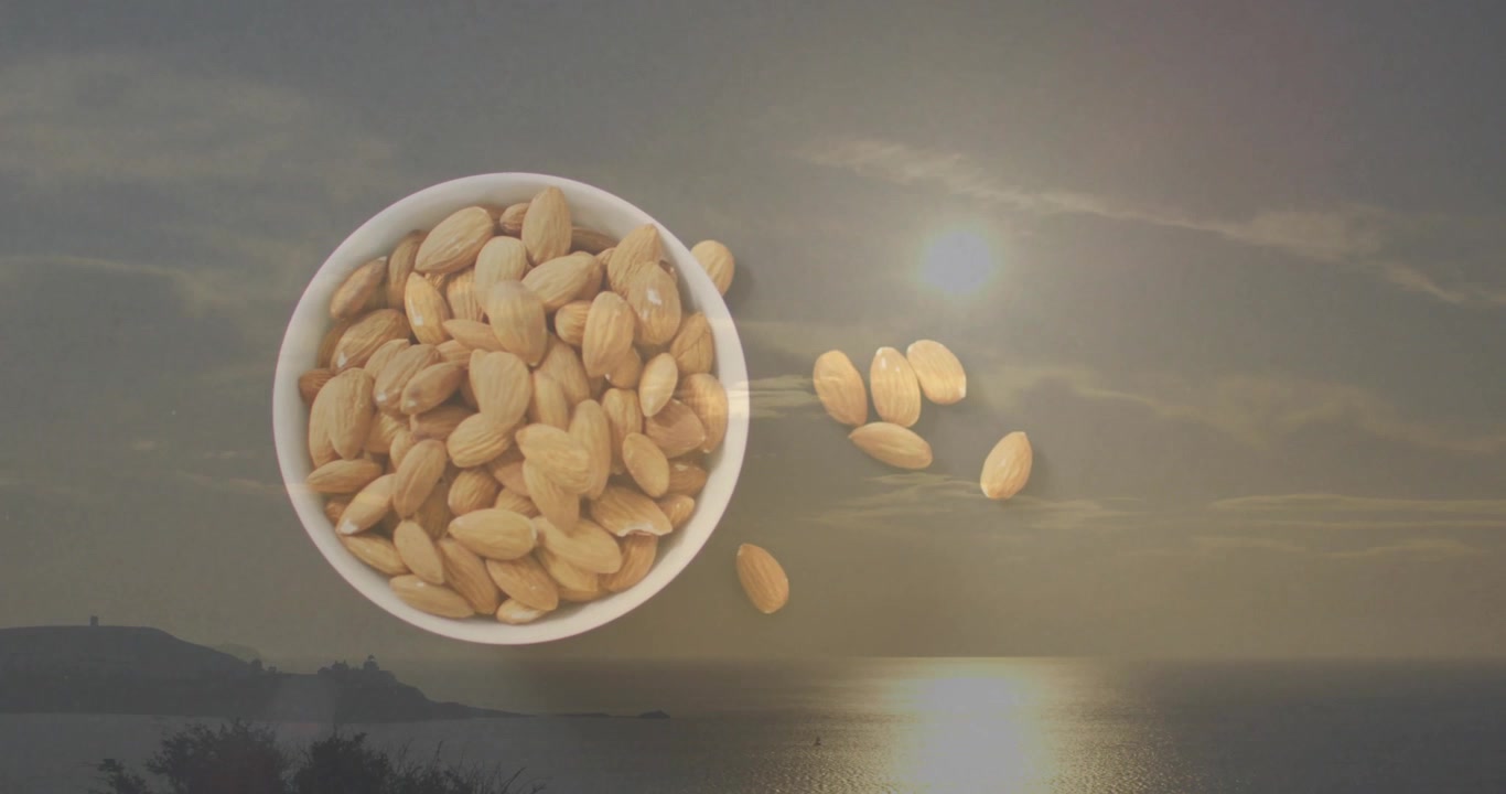 Almonds in bowl with serene sunset reflecting on calm ocean water