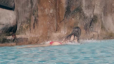 la chica yace en el agua clara de la piscina bajo los chorros que caen.