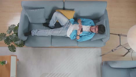 vista superior zoom shot de un hombre acostado en el sofá y usando teléfono inteligente en casa