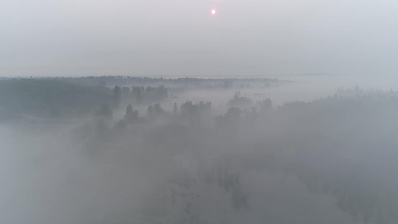 수평선에 붉은 태양이 있는 시골 앨버타의 안개, 연기, 구름 사이로 날아가는 공중 전망