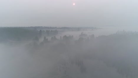 Aerial-view-flying-through-fog,-smoke-and-clouds-in-a-rural-Alberta-with-a-red-sun-on-the-horizon