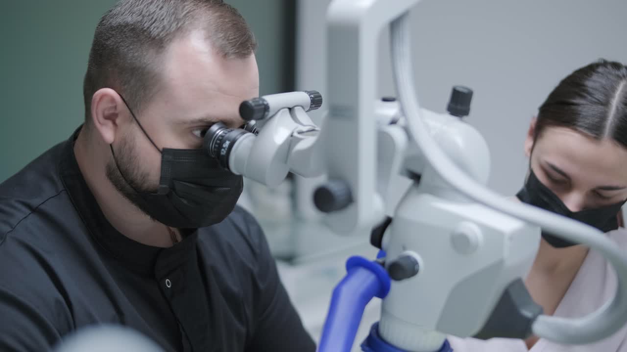 Male dentist working with dental microscope in modern stomatology clinic. Doctor using microscope for root canal treatment. Stomatologist performs a surgical operation. Cosmetic dentistry and surgery.