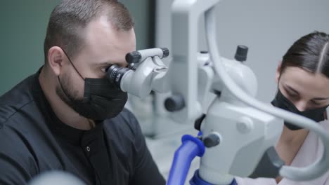 male dentist working with dental microscope in modern stomatology clinic. doctor using microscope for root canal treatment. stomatologist performs a surgical operation. cosmetic dentistry and surgery.