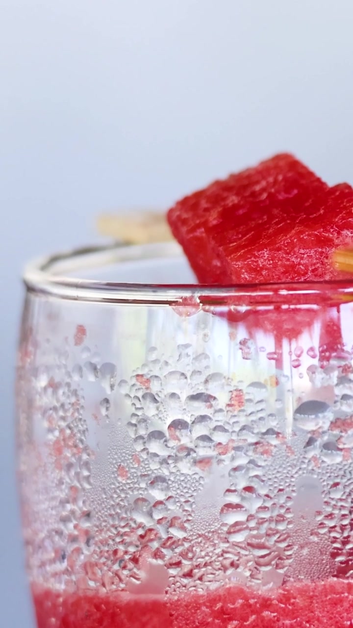 Primo piano estremo di un bicchiere freddo con goccioline d'acqua e una guarnizione di una fetta fresca di anguria.