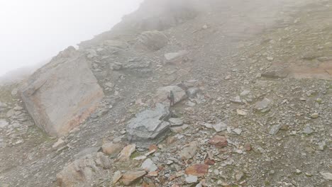 Luftaufnahme-Eines-Einsamen-Wanderers,-Der-Im-Dichten,-Dunstigen-Nebel-Auf-Einem-Felsigen-Berghang-Steht