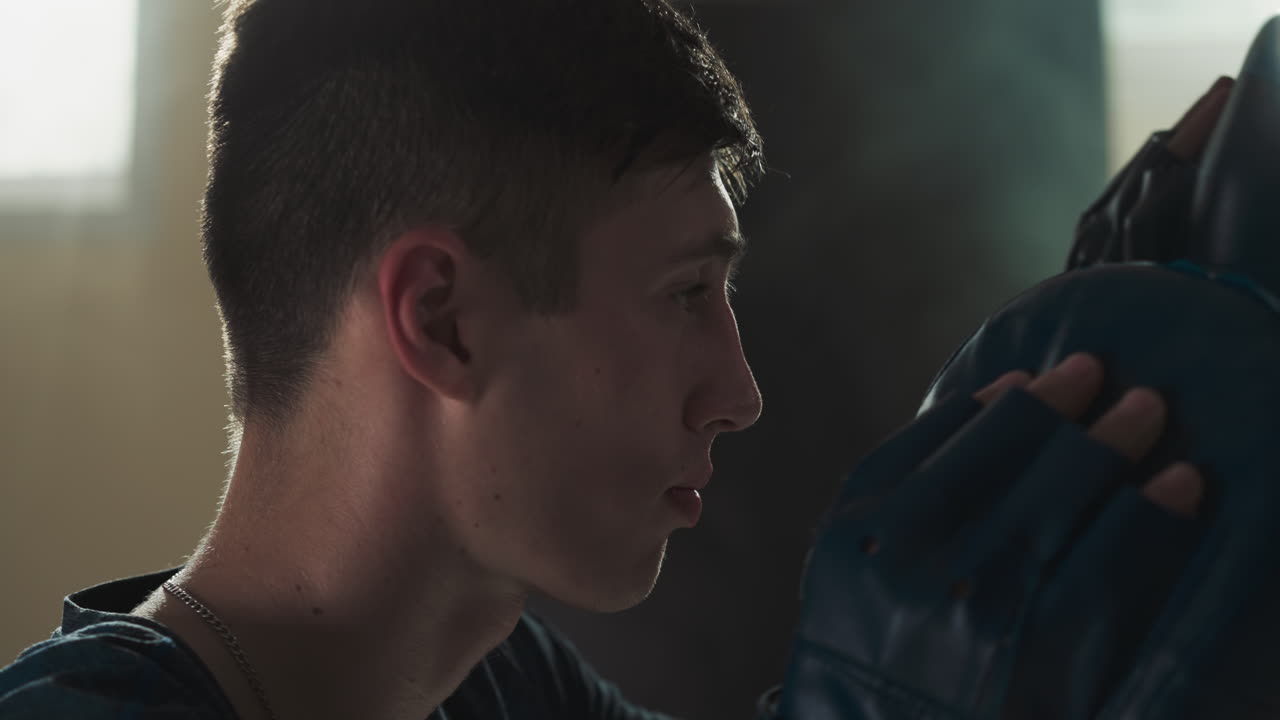 atleta con almohadillas de perforación en el gimnasio de primer plano. joven deportista sostiene el inventario de ejercicios para luchar sparring en el club de cámara lenta. ocio activo