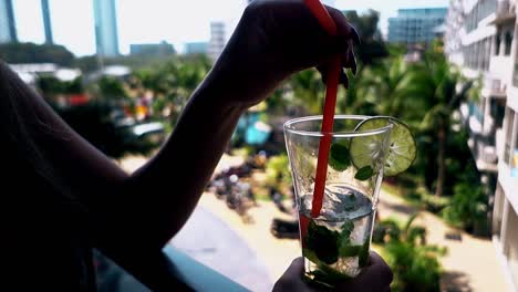 woman holds straw in half empty glass with mojito cocktail