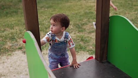 charming baby boy climbing by the wooden steps to the slide. toddler playing on the playground in summer. view from top.
