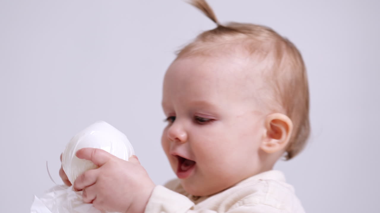 Beautiful one-year-old Caucasian child wearing light shirt. Lovely baby portrait in studio at white backdrop. Close up.