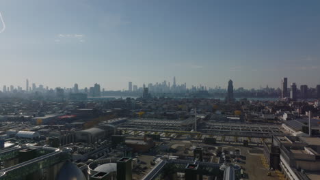 Volar-Hacia-Atrás-Sobre-El-Sitio-Industrial.-Grandes-Tanques-En-Forma-De-Huevo-De-Acero-Brillante.-Vista-Del-Horizonte-Rascacielos-Del-Centro-En-La-Distancia.-Brooklyn,-Ciudad-De-Nueva-York,-Estados-Unidos