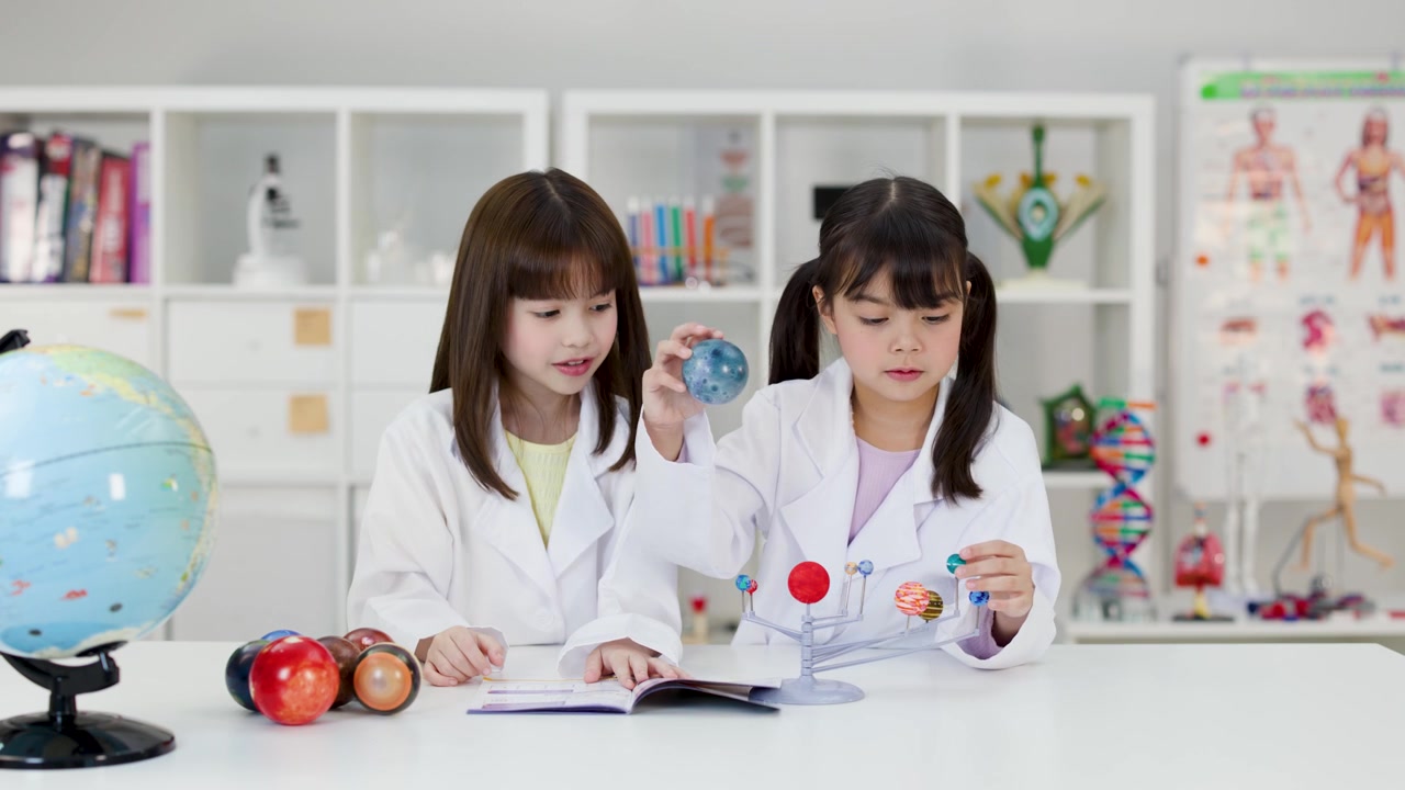 白衣を着た2人の若い少女が、太陽系の模型を使って天文学を学ぶ