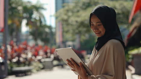 young muslim woman smiling while using a tablet outdoors