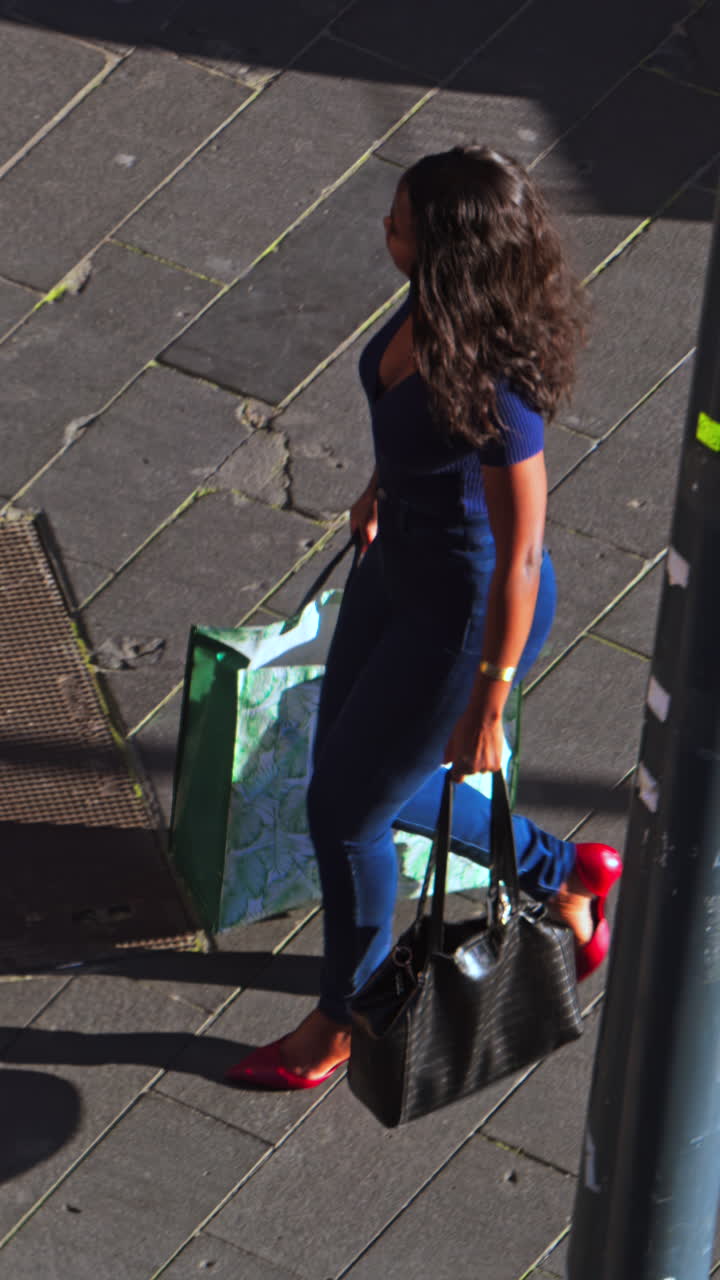 High angle view of a woman walking on the street, holding bags. Vertical
