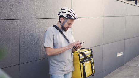 el repartidor de alimentos perdido con una mochila térmica consulta una dirección en su teléfono inteligente porque no sabe dónde está la entrega