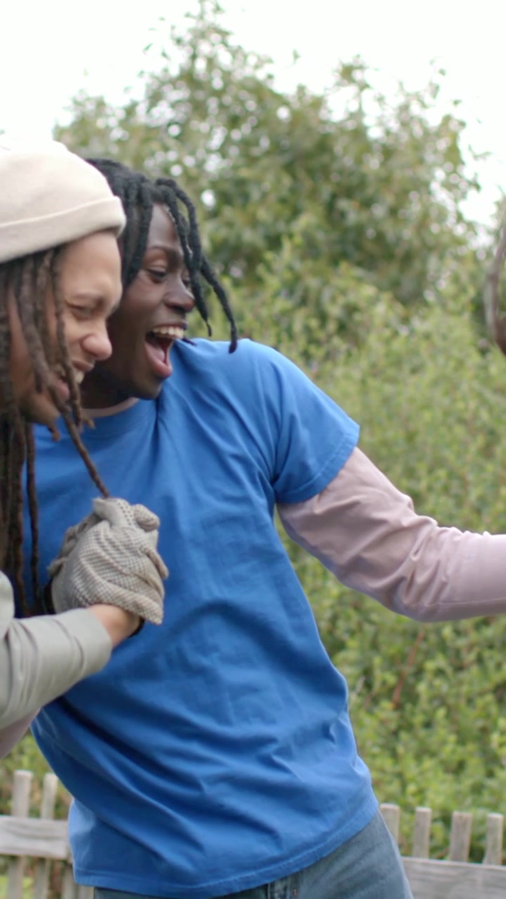 Video vertical: Dos hombres con camisetas azules chocando los guantes, riendo y apoyados en un poste de jardín después del trabajo.