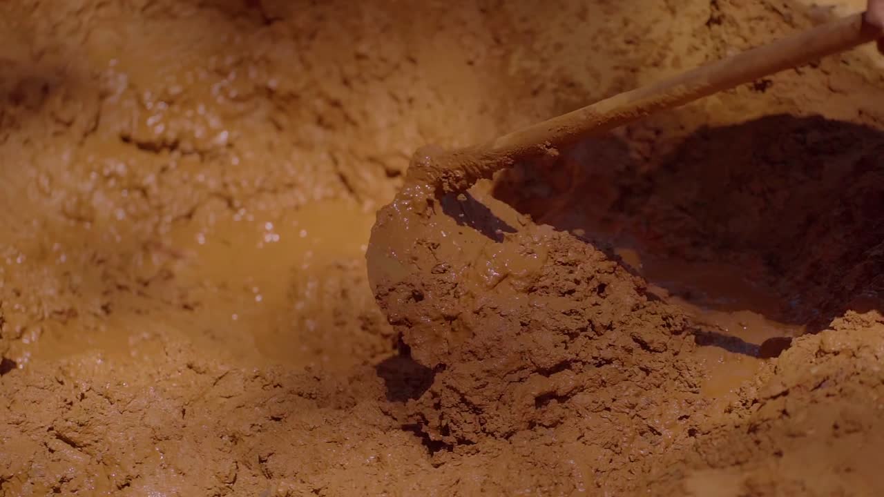 Construction worker blending mud and straw, creating adobe bricks using traditional sustainable method in rural Chapada dos Veadeiros landscape, Brazil, slow motion shot
