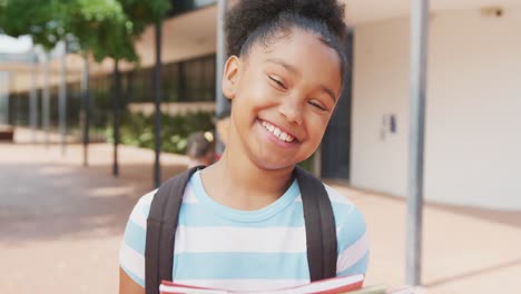 Videoporträt-Einer-Lächelnden-Gemischtrassigen-Schülerin,-Die-Ihre-Bücher-Vor-Der-Schule-Hält